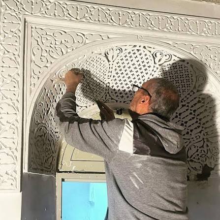 A Moroccan craftsman carving cedar wood in the Fes medina — the hands-on transmission of a craft tradition brought from Al-Andalus in the 15th century and maintained through the master-apprentice relationship for five centuries